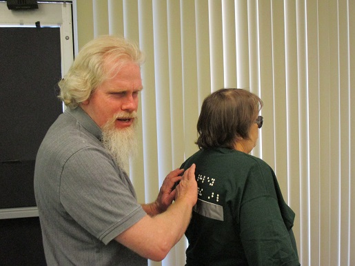 Kelly is trying to read what is on the back of Teresa's T-shirt.